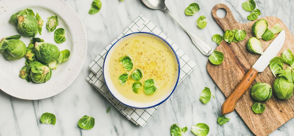 Brussels sprout soup, garnished with fresh sprouts, next to wooden board, wide composition