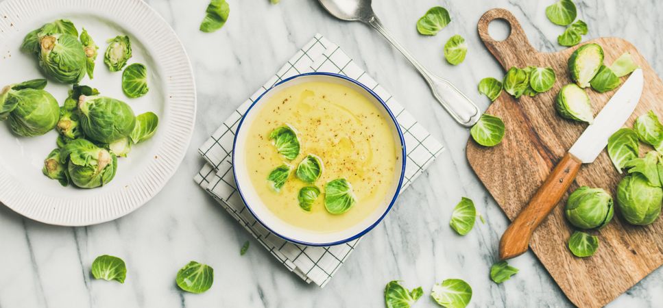 Brussels sprout soup, garnished with fresh sprouts, next to wooden board, wide composition