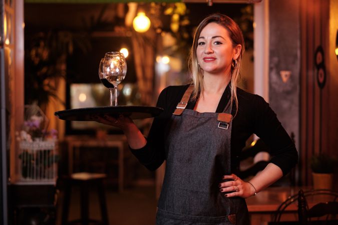 Cheerful waitress holding tray with wineglasses