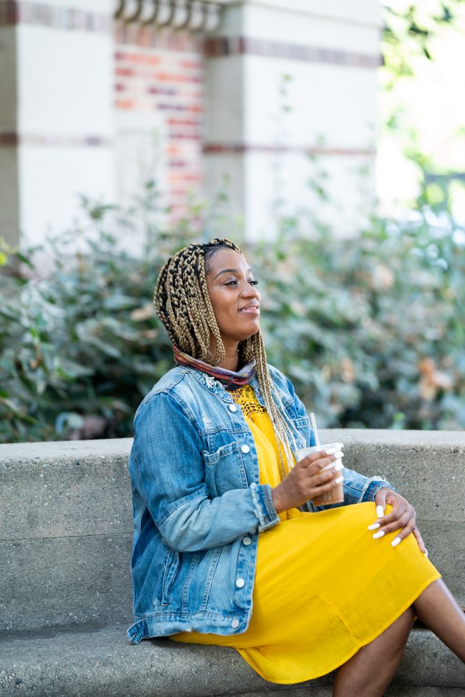 Woman sitting on stone bench with mask around her neck smiling and looking away
