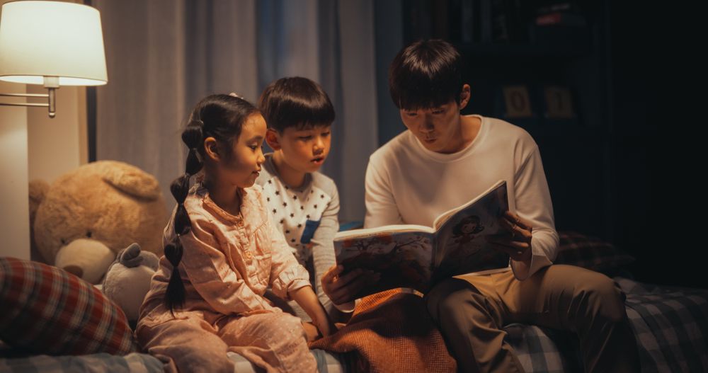 Portrait of Two Active Children Engaged in a Conversation with their Father While He Reads to them Before Bed.
