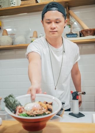 Asian cook holding bowl of ramen