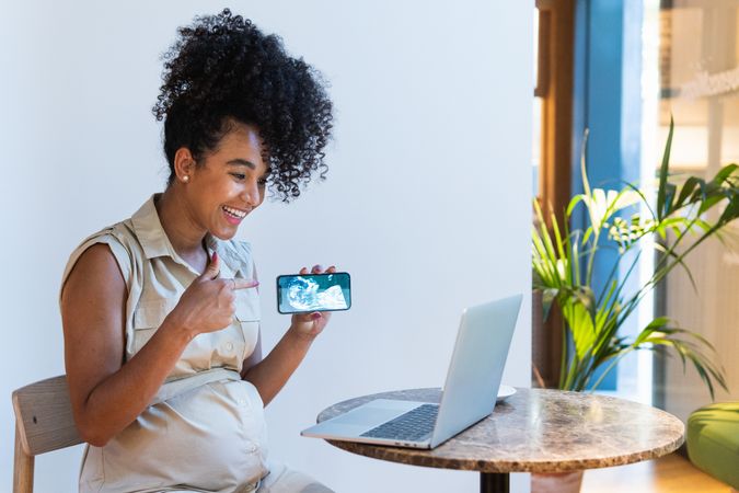 Smiling Black pregnant woman showing baby ultrasound picture to laptop