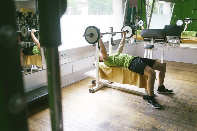 Side view of man in green t-shirt lifting heavy bar exercising arms and chest
