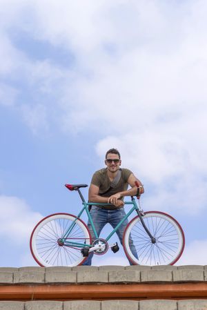 Male standing with bike on roof with beautiful blue sky and clouds, copy space