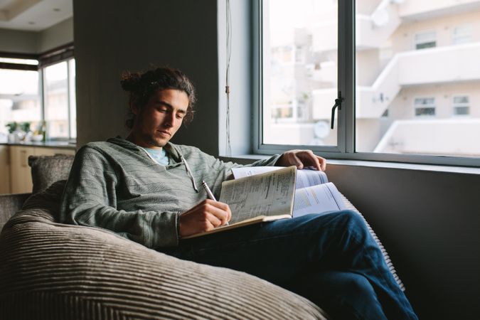 Relaxed student doing homework from home using textbook