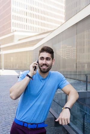 Happy man leaning on glass railing outside talking on mobile phone