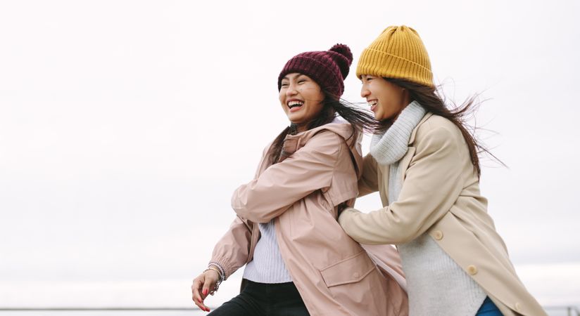 Two happy young women in winter clothes against gray sky