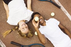 Portrait of two women laying on a tennis court.