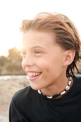 Boy wearing shell necklace looking away at beach