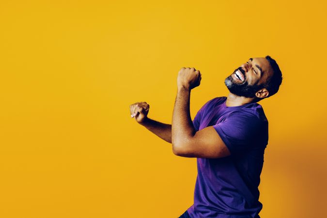 Happy Black man in yellow studio dancing with his head back, copy space