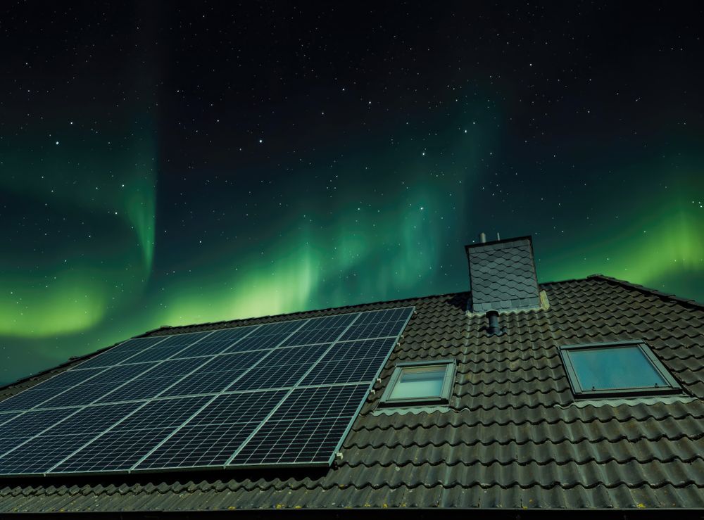 Solar panels producing clean energy on a roof of a residential house with aurora borealis in the background.