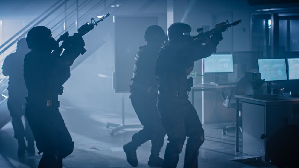 Shot of Masked Squad of Armed SWAT Police Officers Storm a Dark Seized Office Building with Desks and Computers.