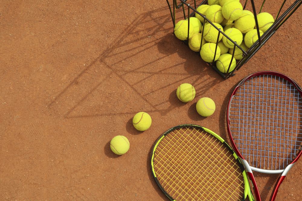 Rackets and basket with tennis balls on clay court