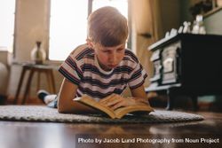 Boy relaxing on a carpet and reading a book at home 56ZLd5