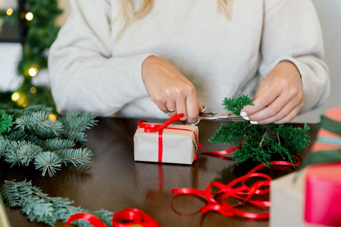 An unrecognizable woman is wrapping a Christmas gift in craft paper and a fir branch
