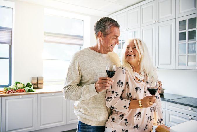 Smiling older couple in a bright kitchen with red wine