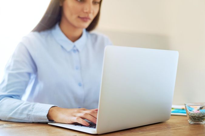 Close up of woman in blue shirt working on laptop on wooden desk