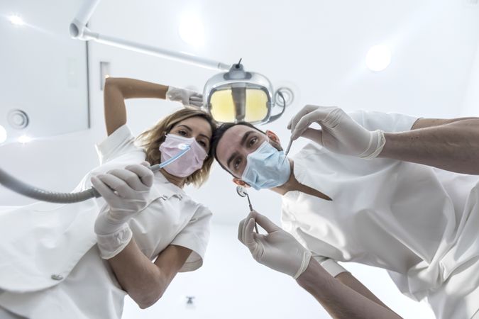 Low angle portrait of male and female dentists wearing masks at dental clinic during exam