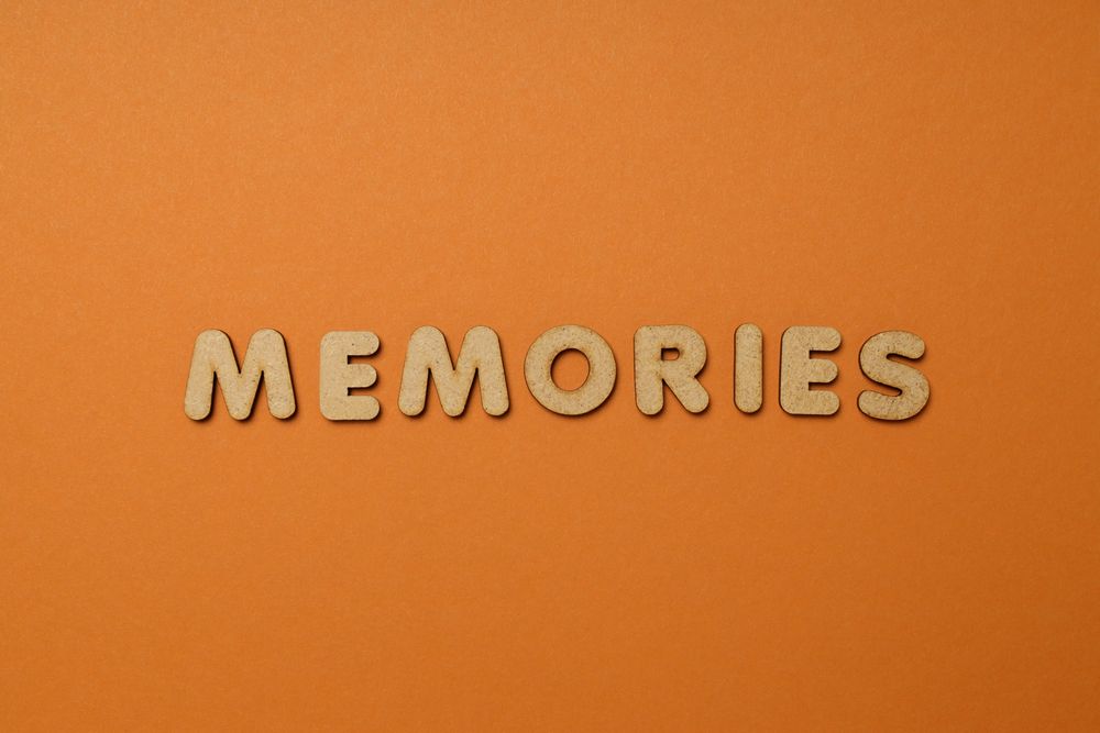The word “Memories” written in cork in center of dusty orange background, copy space