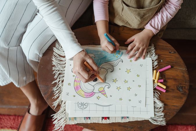 Cropped image of adult and child drawing and coloring with crayon