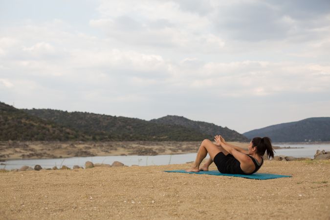 Woman practicing yoga outdoors near water