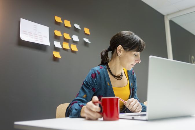 Businesswoman with hot beverage using laptop