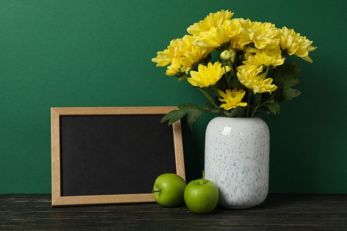 Apples, vase with flowers and empty frame on green background, space for text