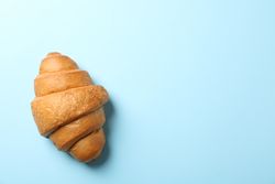 Freshly baked croissant on blue background, top view, copy space