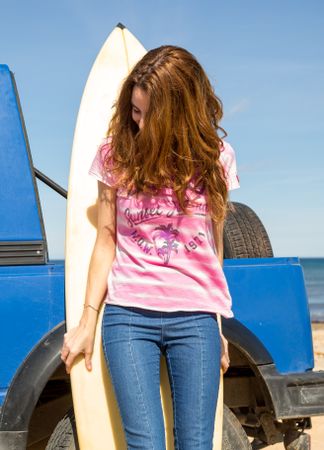Woman leaning on surfboard near car at seaside