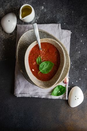 Top view of traditional Spanish gazpacho with basil leaf and olive oil garnish in grey ceramic bowl