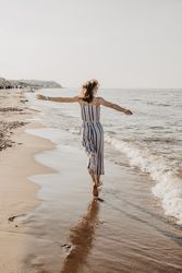 Back view of blonde woman in striped jumpsuit running on seashore 0yGB14