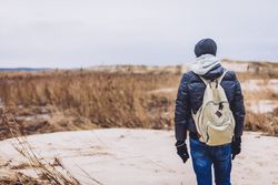 Man walking between sand field with dry grass