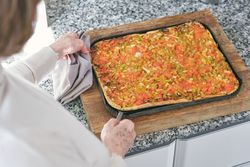 Unrecognizable woman taking out pizza from baking pan