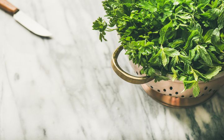 Top view of colander full of fresh green herbs with knife, horizontal composition, copy space