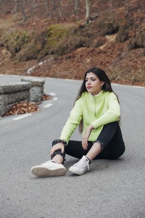 Woman in sweater sitting on asphalt road