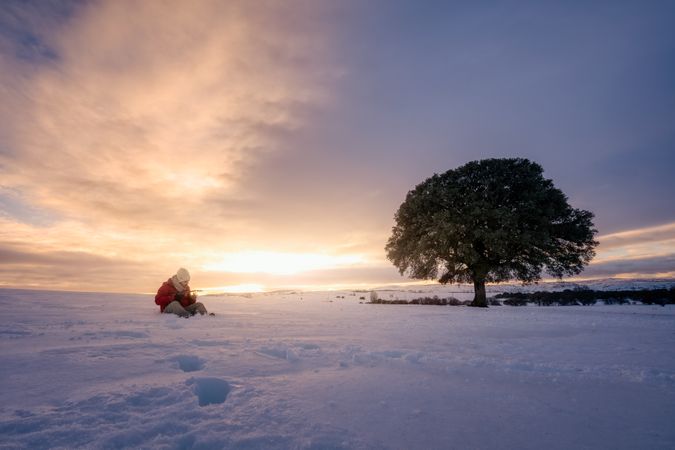 Person sitting on snow against sunset sky playing guitar