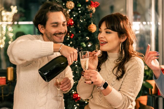 Happy young couple celebrating Christmas by pouring champagne together.