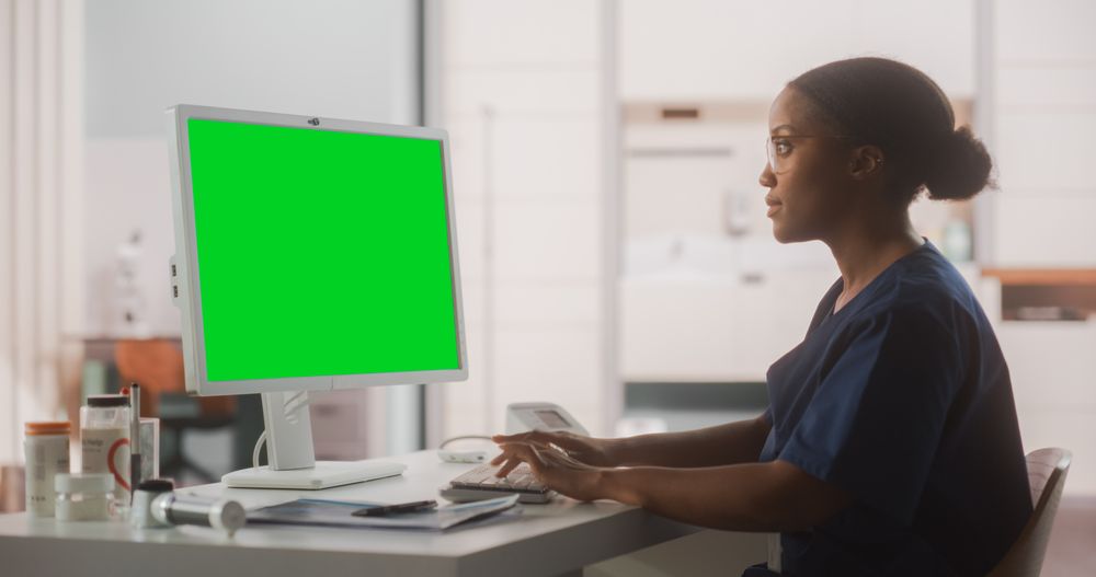Portrait of a Black Female Medical Health Care Professional Working on Desktop Computer with Green Screen Mock Up Display in Hospital Office.