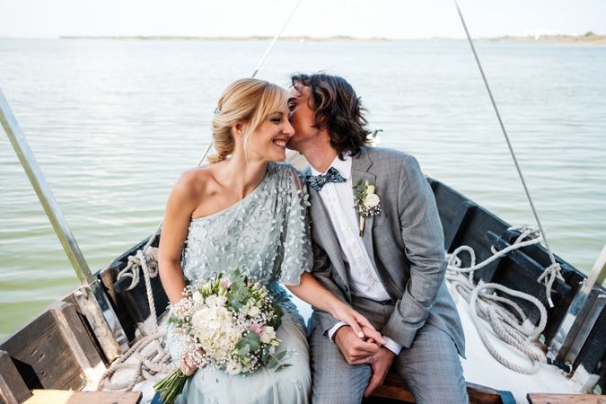 Content newlyweds smiling and holding hands while sitting on boat