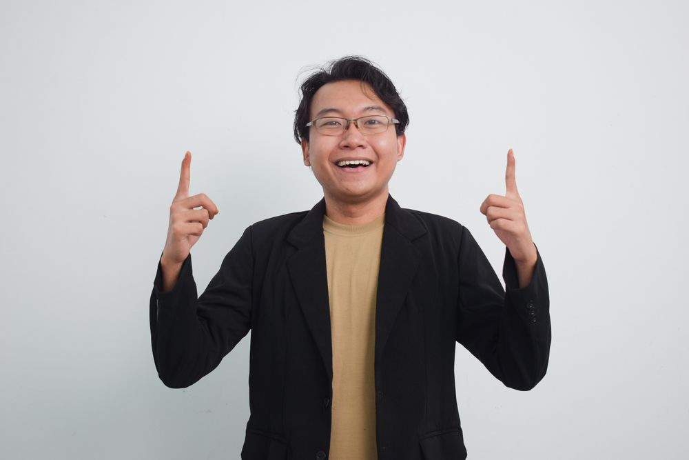 Joyful Asian businessman with suit and casual shirt pointing up