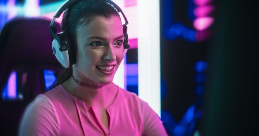 Stylish Young Woman Playing Video Games on a Desktop Computer in a Technologically Advanced Room with Futuristic Neon Background.