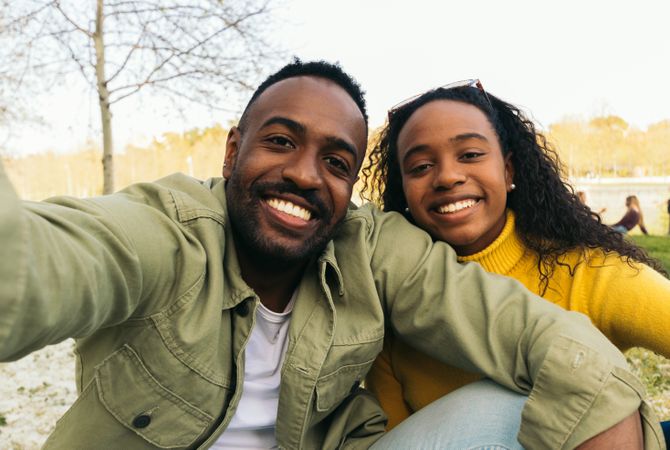 Black couple taking a selfie sitting in a park