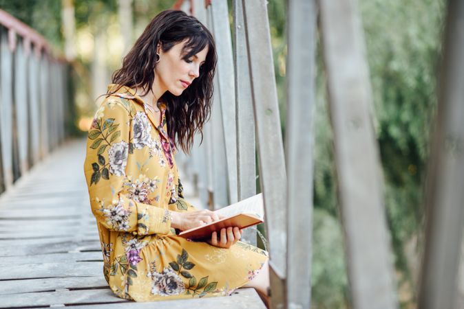 Calm female sitting on a rural bridge and reading