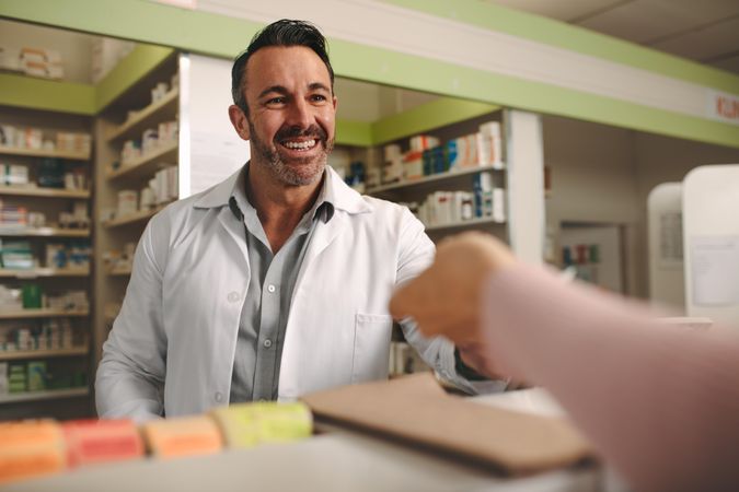 Customer handing a medical prescription to the smiling male chemist standing behind counter
