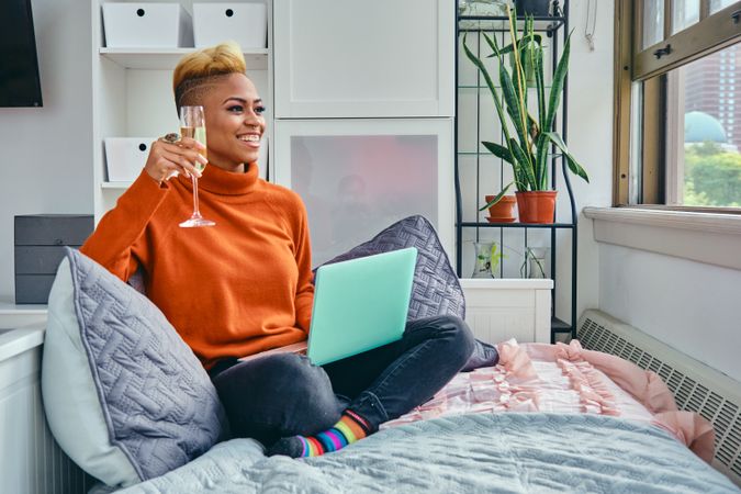 Smiling Black woman with a laptop and champagne in a bright modern home