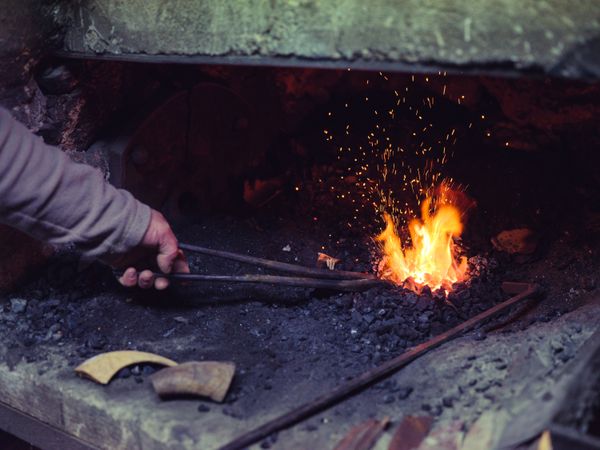 Crop faceless farrier melting metal in furnace in smithy