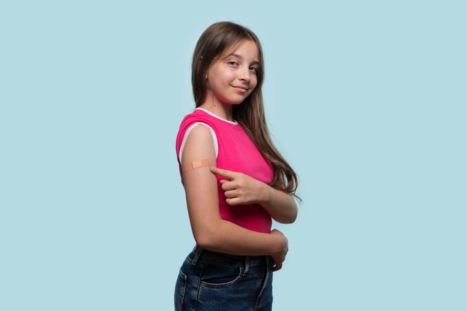 Girl showing arm bandage with OK gesture after vaccination.