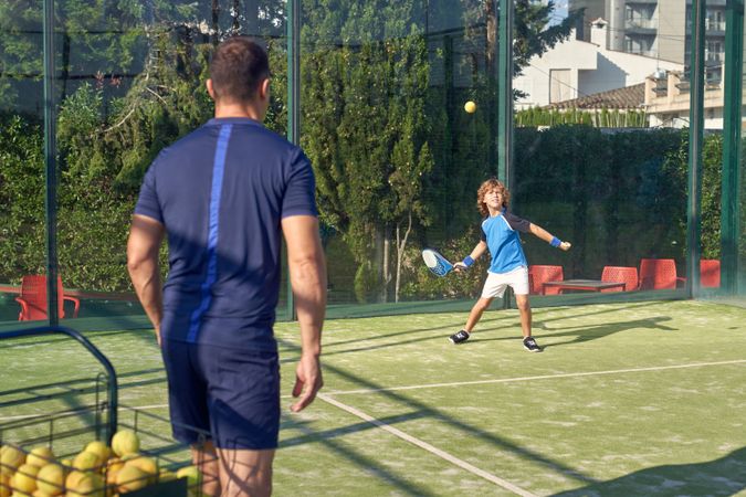 Trainer near boy playing padel