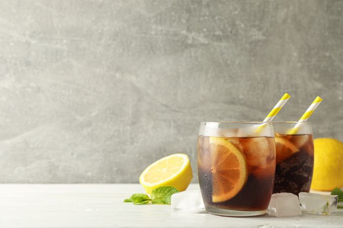 Glasses with cold cola and citrus on white cement background, space for text